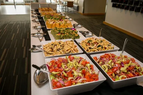 Buffet line with pasta salads, wraps and fresh vegetable salads in white serving bowls
